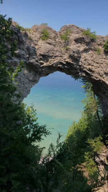 A natural rock arch frames the blue water and green trees at Mackinac Island, HD Phone Wallpaper