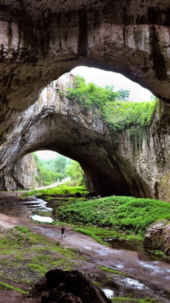 A person walking under natural rock arches surrounded by greenery in Bulgaria Wallpapers, HD Mobile Wallpaper