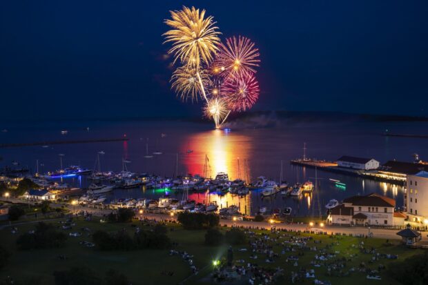 Fireworks light up the night sky over the Mackinac Island harbor with boats and crowds watching, 2K Desktop Wallpaper