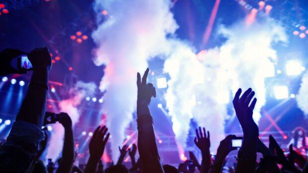 A lively nightclub crowd raising hands amid colorful lights and smoke effects, 4K Desktop Wallpaper