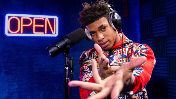 Nle Choppa performing in a recording studio with a colorful jacket and headphones on