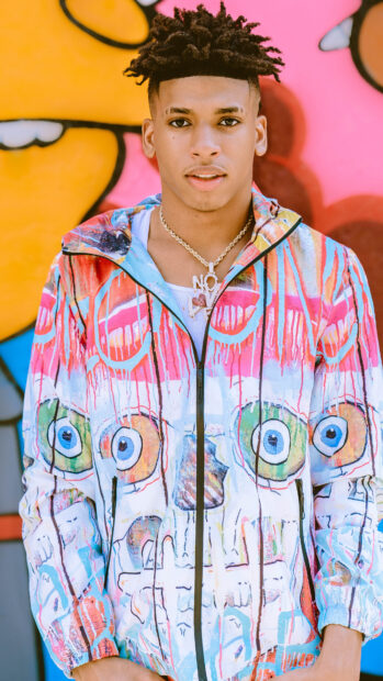 Young man wearing colorful jacket with skull art standing against graffiti wall with vibrant colors