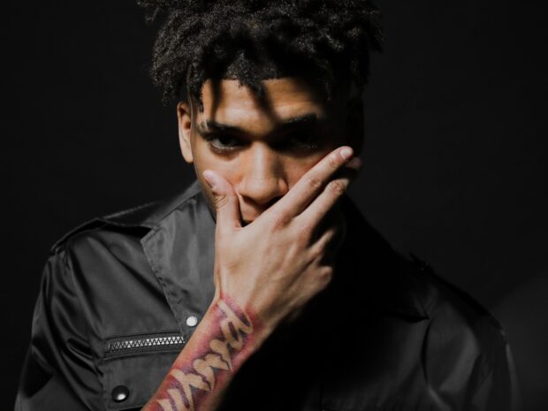 Nle Choppa showing his tattooed wrist while covering part of his face with his hand