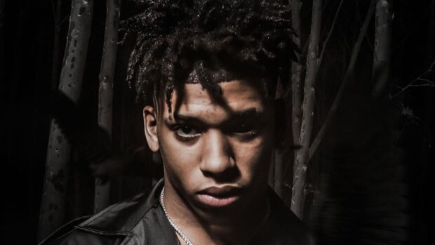 Nle Choppa face close up shot in dark forest with intense expression