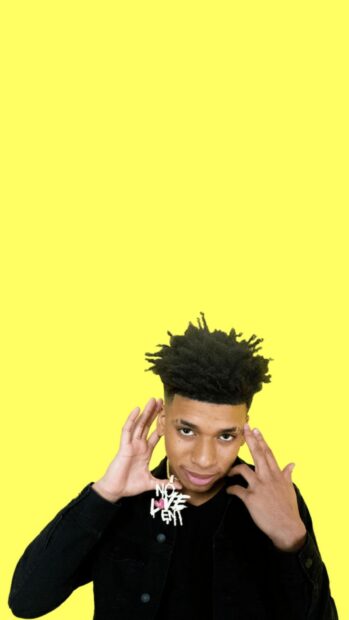 Nle Choppa wearing a black jacket and showing a necklace against a yellow background