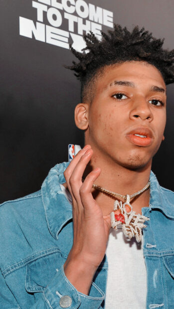 Nle Choppa wearing a denim jacket and holding a gold chain necklace with pendant