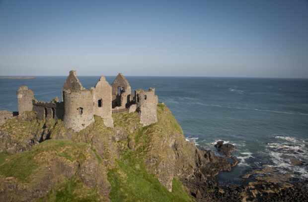 A scenic view of an ancient castle on the Northern Ireland coast with the ocean in the background, 2K Desktop Wallpaper