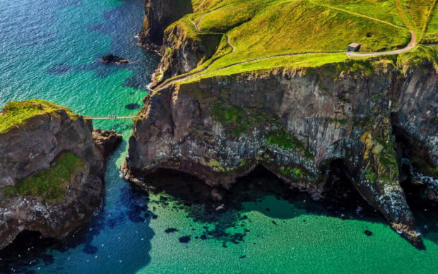 A scenic coastal cliff with green grass and clear water in Northern Ireland, 2K Desktop Wallpaper