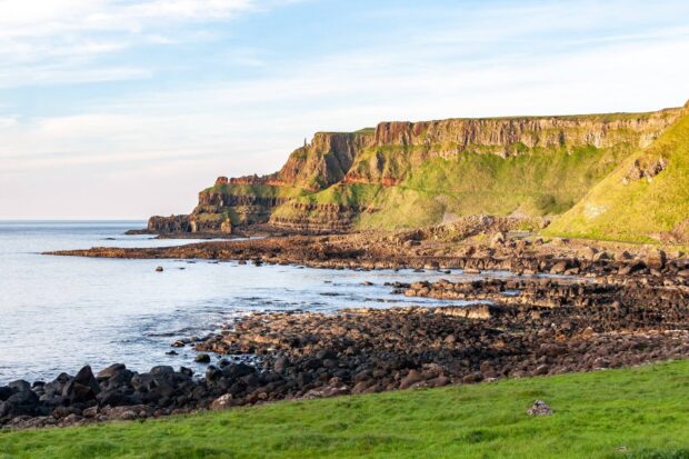 The northern Ireland cliffs rise dramatically above the rocky shore under a clear sky, HD Desktop Wallpaper