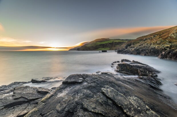 A stunning view of Northern Ireland's rocky coast under a calm sky at sunset, HD Desktop Wallpaper