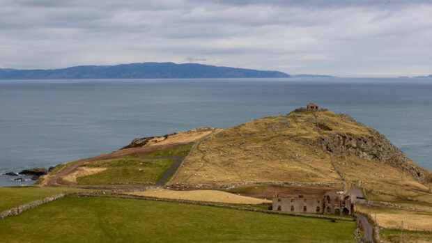 A view of Northern Ireland wallpapers showing a coastal hill and ruins under a cloudy sky, 2K Desktop Wallpaper