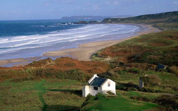 A small house near a sandy beach in Northern Ireland shows a peaceful coastal landscape, 2K Desktop Wallpaper