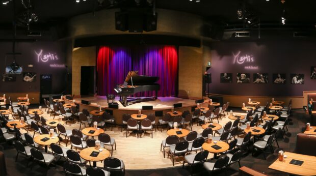 A grand piano on stage with red curtains in a cozy Oakland music club