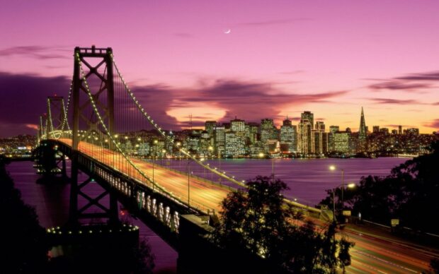 Vibrant twilight view of Oakland bridge and city skyline with glowing lights and pink sky
