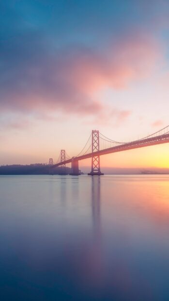 A calm sunset view of Oakland bridge with soft clouds and smooth water reflection