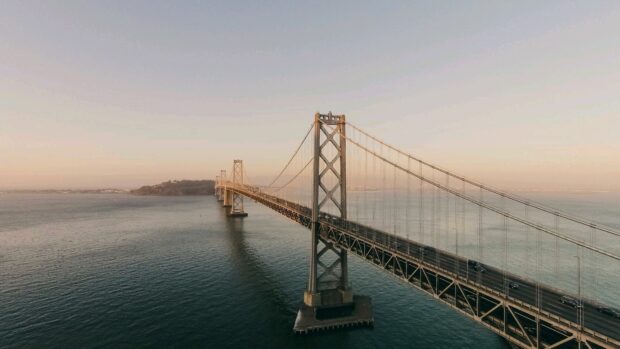 Aerial view of Oakland bridge crossing the calm water at sunset with clear sky