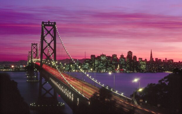 A beautiful view of the Oakland skyline with a bridge at sunset in purple and pink colors