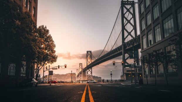 A scenic view of Oakland bridge and street at sunset with cars and buildings