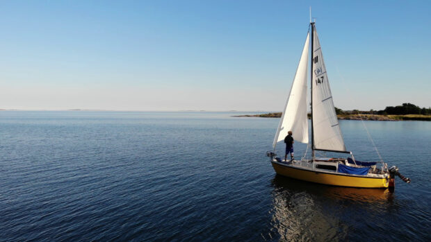 A man stands on a sailboat sailing near the coast of Oland Sweden