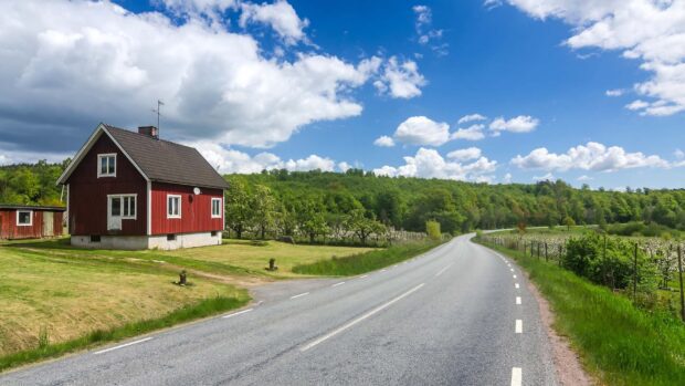 A red house near a winding road in Oland Sweden surrounded by green trees and grass