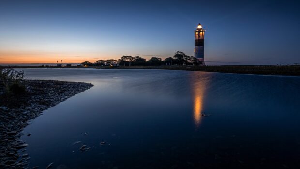 A calm waterfront scene in Oland Sweden with a lit lighthouse reflecting on the water at dusk