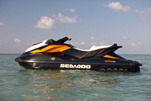 A Sea Doo jet ski floats calmly on the clear ocean water under a blue sky with clouds, 2K Desktop Wallpaper