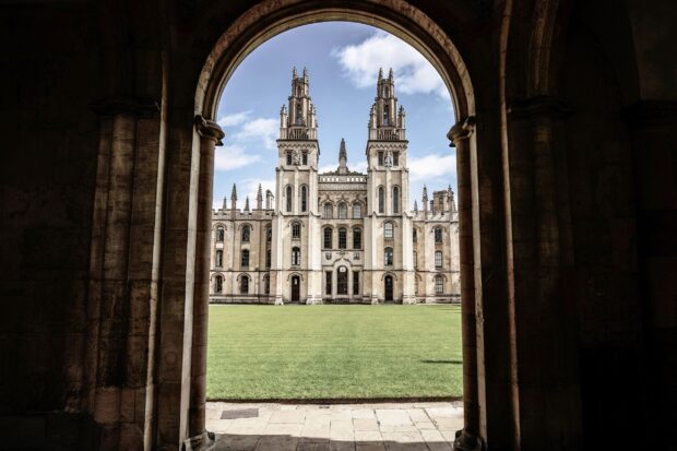 A grand view of Oxford University is framed by an arch with a green lawn under blue sky, 2K Desktop Wallpaper