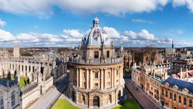 The Radcliffe Camera at Oxford University is surrounded by historic buildings under a blue sky, 2K Desktop Wallpaper