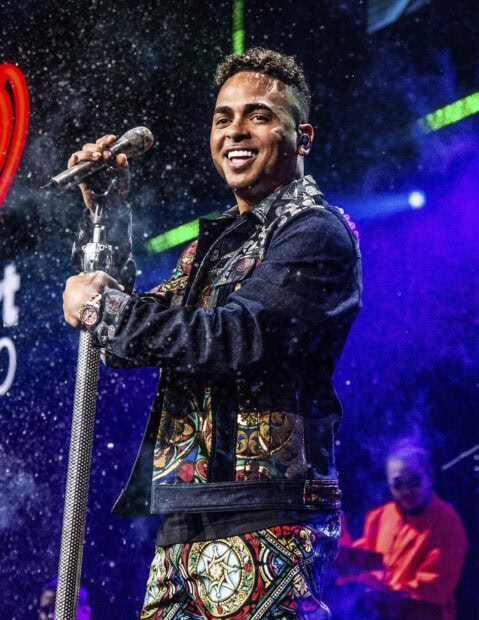 Ozuna is smiling and holding a microphone on stage during a vibrant concert, HD Mobile Wallpaper