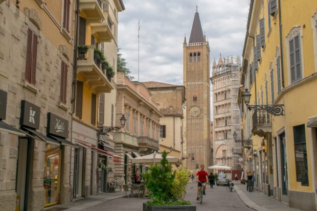 Historic street and clock tower in Parma Italy city center with people walking and cycling