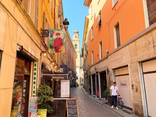 Narrow street with colorful buildings and a person walking in Parma Italy
