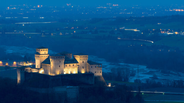 The illuminated Parma Italy castle surrounded by countryside at dusk