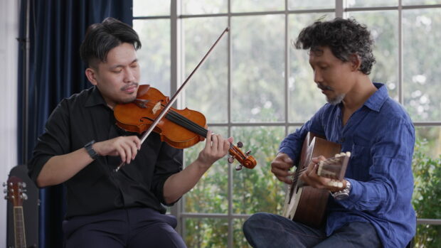 A man passionately plays the violin with a focused expression while another plays guitar, 4K Desktop Wallpaper