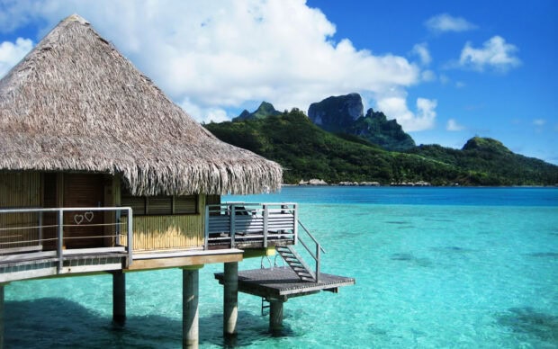 A bungalow stands over turquoise water with lush green mountains in the background, HD Desktop Wallpaper