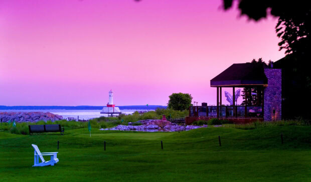 A serene view of green grass and a lighthouse at Mackinac Island during sunset, 2K Desktop Wallpaper