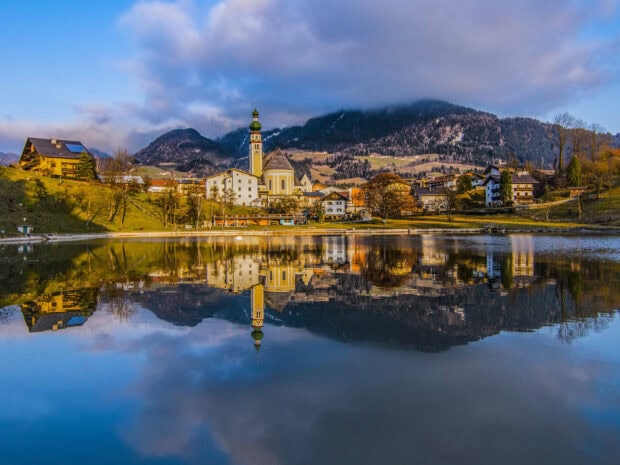 A peaceful village with a church reflecting on a calm lake in Austria, HD Desktop Wallpaper