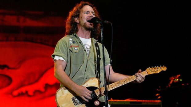 The lead singer of Pearl Jam plays guitar during a concert with a red background, HD Desktop Wallpaper