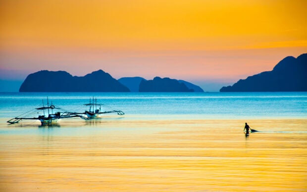 A fisherman near boats with scenic islands in the Philippines at sunset