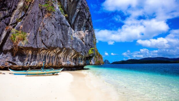A traditional boat resting on the beach near limestone cliffs in the Philippines