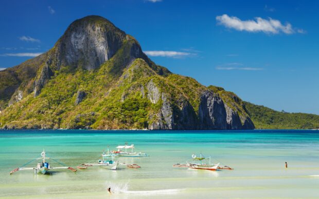A beautiful view of a Philippine island with traditional boats in clear turquoise water
