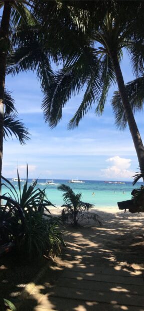 Tropical palm trees framing a beach scene in the Philippines with clear blue water and boats in the distance