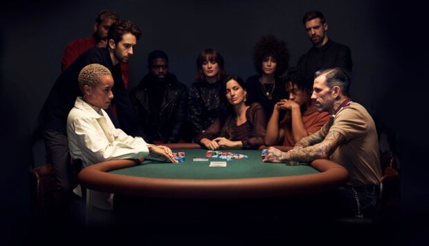 A group of people focused on playing poker at a green felt table in a dimly lit room