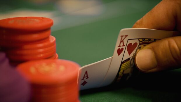 A poker hand with an ace and king being held near poker chips on a green table