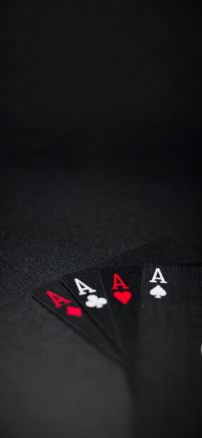 A set of four poker cards with aces of different suits on a black surface