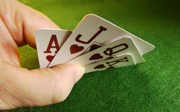 A hand holding a poker royal flush hand of hearts on a green felt table