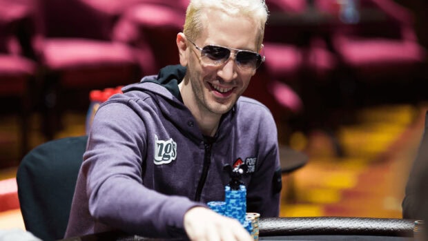 A poker player wearing sunglasses and a hoodie smiling while playing poker chips on the table