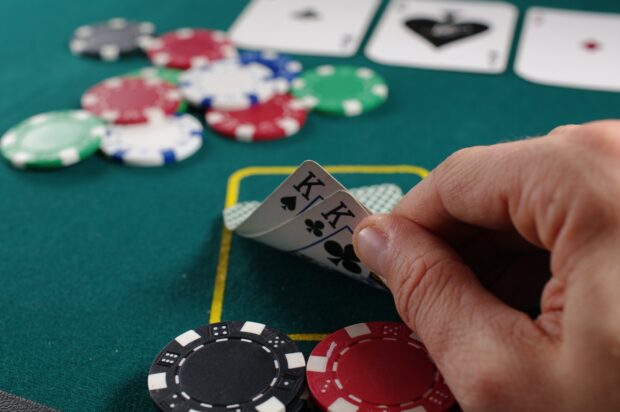 A hand holding two kings poker cards with casino chips on the table
