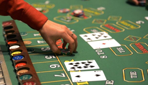A hand placing poker chips on a green poker table with playing cards and chips displayed