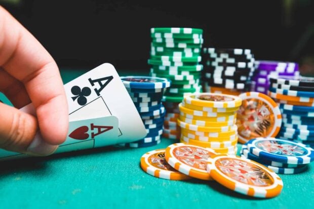 A hand holding poker cards with poker chips stacked on a green table