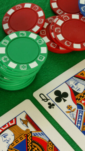 Close up of poker chips and playing cards showing the queen of clubs on a green felt table